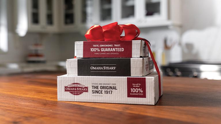 A stack of Omaha Steaks boxes wrapped in a red ribbon sitting on a wooden table