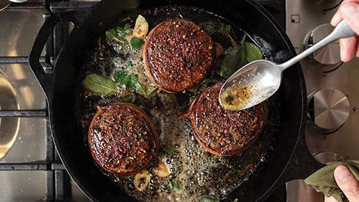 three bacon-wrapped filet mignons cooking in a cast iron skillet
