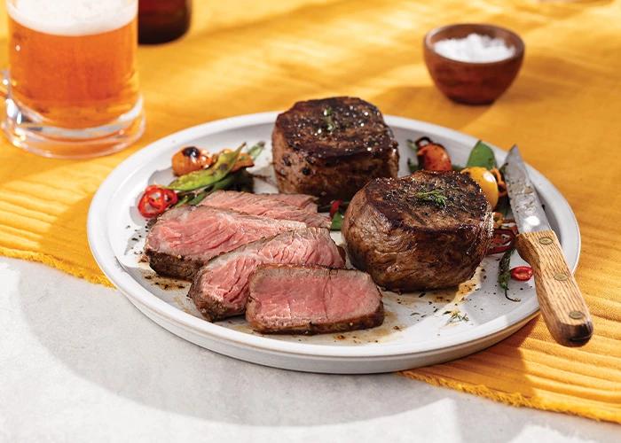 Seasoned, grilled filet mignon, sliced on a plate, garnished with tomatoes.